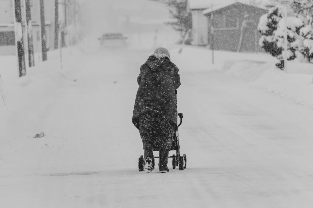 雪の中道路の真ん中を歩く高齢者